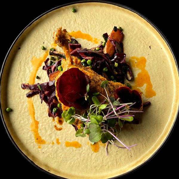 Gourmet dish with golden-brown chicken, red cabbage, green peas, and microgreens on a beige plate.