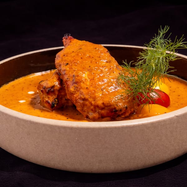Two pieces of chicken in a rich orange sauce, garnished with dill and cherry tomatoes.