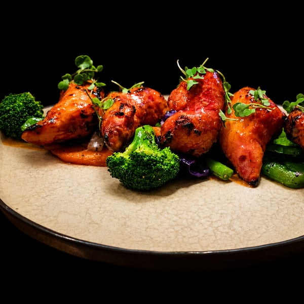 Glazed chicken pieces with broccoli, green beans, and orange puree on a textured plate.