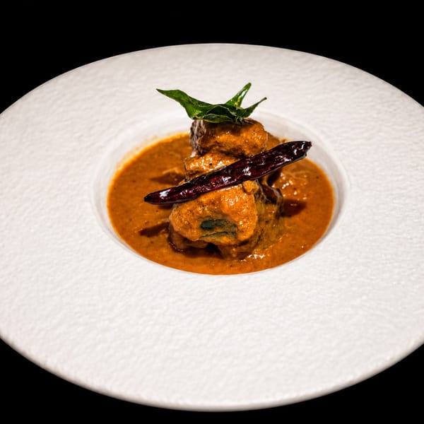 Indian dish with meat in a rich orange sauce, garnished with green leaves and a dried red chili.